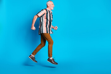 Full length photo of positive cheerful man wear striped trendy clothes run empty space isolated on blue color background