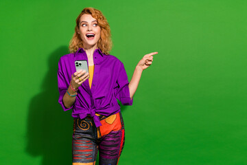Photo portrait of pretty young girl point excited empty space hold gadget wear trendy purple outfit isolated on green color background