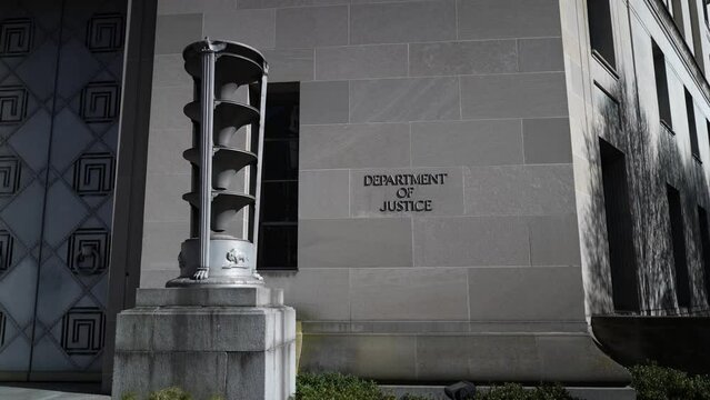 Push in to the entrance to the Department of Justice with sign on building entrance in Washington, DC.