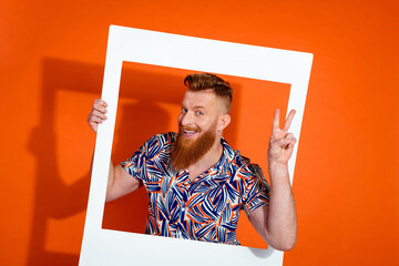 Photo of funky cool positive guy with red beard wear print shirt in frame showing v-sign symbol...