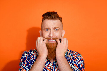 Photo of nervous scared guy dressed print shirt biting fingers emtpy space isolated orange color background