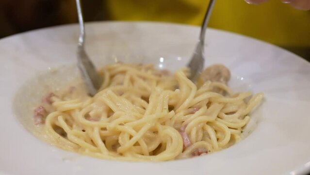 using fork to eat fresh pasta carbonara spaghetti with white sause and ham bacon, home made traditional italian dinner on restaurant kitchen, tasty food