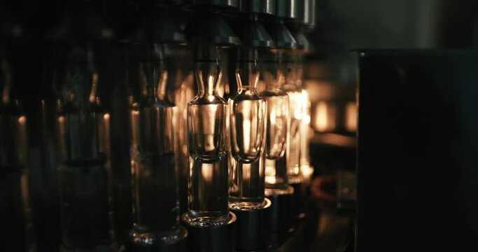 A series of glass bottles are being filled with liquid in a bottling factory. The plastic bottles are all the same size and shape inside the bottling machine are all lined up in a row in the industry.