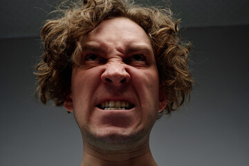 Low angle closeup studio portrait of angry young Caucasian man with teeth clenched, gray...