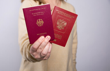 Close up of a woman in yellow sweater holding a German and a Russian passport