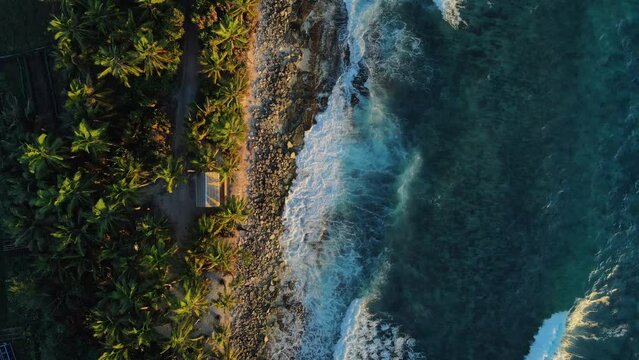 Ocean coastline with house, ocean waves and sunrise or sunset tones at tropical island. Aerial top down view
