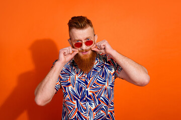 Photo of brutal stylish guy with red beard in sunglass touching mustache advertising barershop isolated on orange color background
