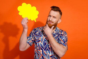 Photo of minded smart guy with red beard wear print shirt holding mind cloud hand on chin isolated on vivid orange color background