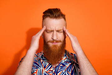 Photo of tired upset guy dressed print shirt smiling hands head feeling headache isolated orange color background
