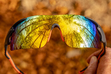 one hand holds a pair of cycling glasses reflecting a beautiful autumn forest
