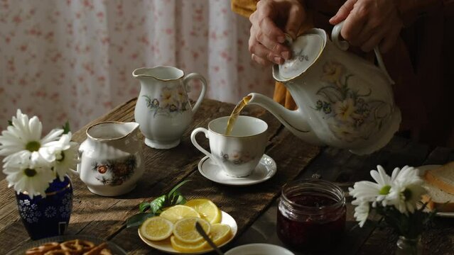 Tea party in rustic house. Pouring tea from teapot into porcelain cup.