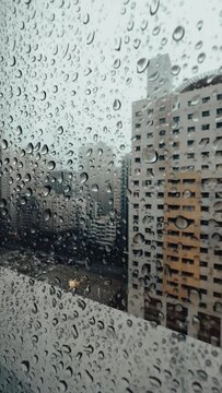 Rain falling on window in skyscraper apartment. Dark and stormy rainy day in big city life. View of dreary Hong Kong cityscape whilst rain drops fall on the window. Abstract somber moody background. H