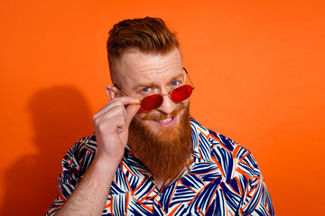 Photo of nice cool guy with red beard trendy haircut wear stylish shirt touch sunglass smiling isolated on vibrant orange color background