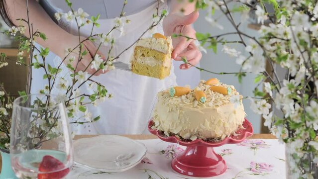 Large cake with cream and almond crumbs: inside with carrot cakes. Cake on the table with spring decor. Dark cake close-up, a woman cuts it with a knife. High quality FullHD footage