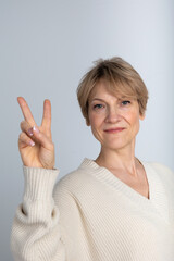 Portrait of emotional woman. Woman's hands gesturing peace sign or victory on light grey background. Looking at camera. High quality photo