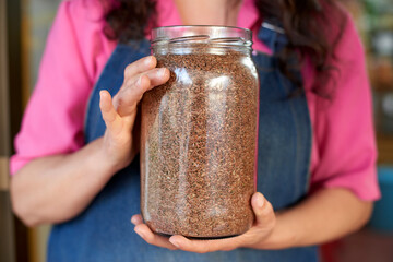 Apron-clad person holds a clear jar brimming with organic brown flaxseeds