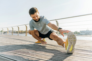 A dedicated athlete stretches on a boardwalk, focusing intently on his form against a backdrop of a...