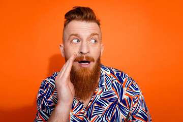 Photo of excited positive guy dressed print shirt telling secret looking emtpy space isolated orange color background