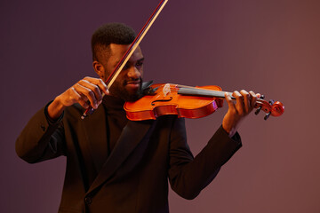 Talented African American man in suit playing violin on vibrant purple background in studio setting