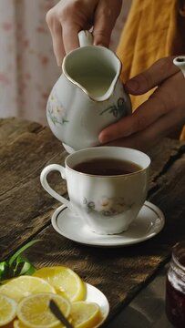 Vertical video. Tea party in rustic style. Pouring milk into tea cup.