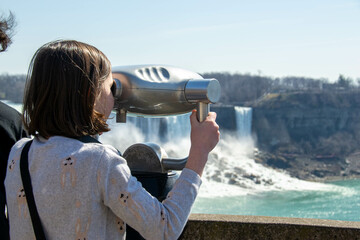 Boy looking through the viewing binoculars on the balcony across the American and Bridal Veil Falls...