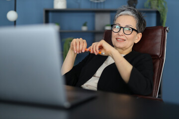 A professional businesswoman, smiling, works on her laptop in a modern office, embracing success and positivity.