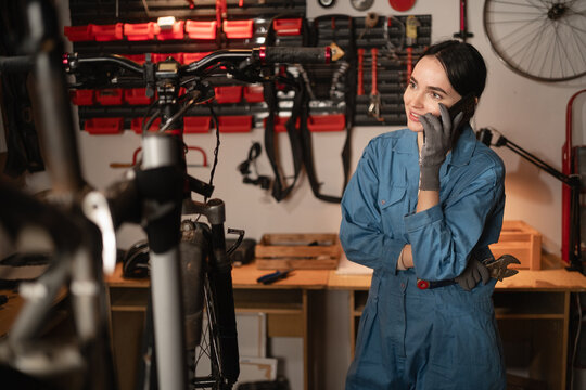 Female mechanic talking on mobile phone. Girl calls after fixing bike in atmospheric garage - Powered by Adobe