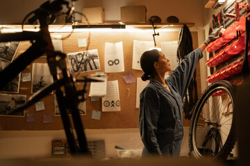 Serious repairwoman in bicycle workshop looking on wall with equipment. Bike mechanic and confident...