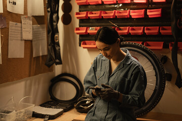 Girl mechanic repairing a bike in a workshop or garage using a smartphone to find the problem of a broken bicycle
