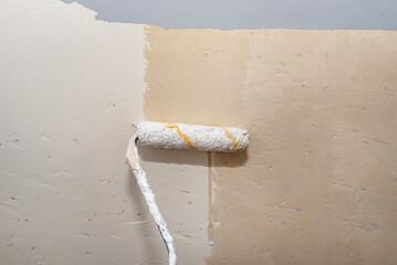 Preparing damaged and holes in walls for painting, scratched by dog claws, applying a priming layer using a paint roller.