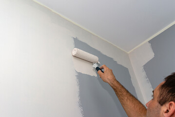 Painter paints a room in beige color using a paint roller at home.