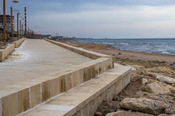 Construction of an embankment by the sea. Landscaping of the coastal area. Buildings near the shore. The embankment is made of blocks of natural hewn stone.