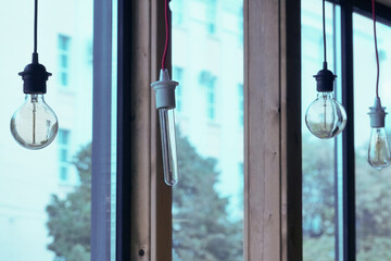 Naklejka premium Vintage light bulbs suspended from a wire. Hanging retro incandescent lamps. The view from the window. closeup of photo 
