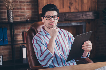 Photo of nice young corporate man think hold clipboard wear striped shirt loft interior office...