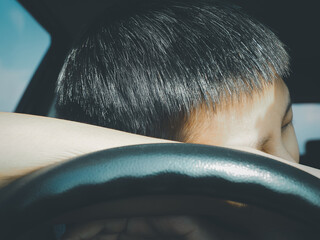 A young Asian man falls asleep at the wheel of his car while taking a break from driving on the...