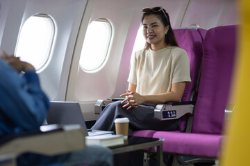 Young Asian woman and friends sitting talking and taking travel photos while in flight. Young...