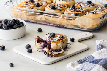 A torn fresh baked blueberry cinnamon roll with a tray of baked rolls in behind.