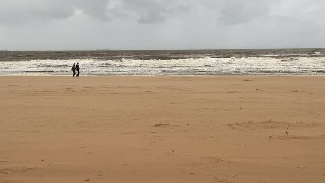 Tourists walk along the shore of a stormy sea