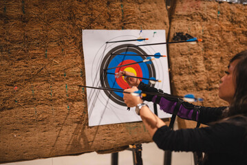 A young Asian woman of novice skill is seen retrieving arrows from a colorful target at an indoor...