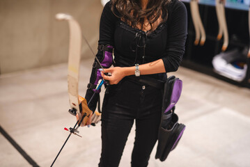 Anonymous shot of a beginner Asian woman practices archery at an indoor range, exploring a new hobby. - obrazy, fototapety, plakaty
