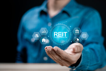 REIT, Real estate investment trust concept. Businessman holding virtual REIT icon on virtual screen for real estate management that generates continuous income.