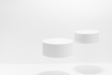 Abstract white scene mockup - two round white cylinder podiums levitate in hard light, shadow. Template for presentation cosmetic products, goods, advertising, design, sale, text in fashion style.