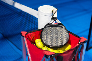 Black professional paddle tennis racket and ball with natural lighting on blue background....