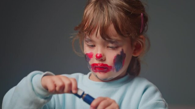 Portrait of little cute girl puts on makeup with adult cosmetics in front of a mirror, playing makeup game indoors