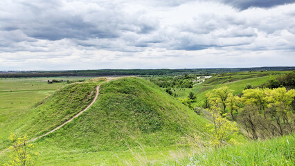 Mountain path through green grassy mountain ridge winding up in to the distant mountain peak under cloudy sky