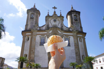 Pao de queijo (Brazilian cheese bun) with the church of Our Lady of Mount Carmel in Ouro Preto, Minas Gerais, Brazil, the city is World Heritage Site by UNESCO