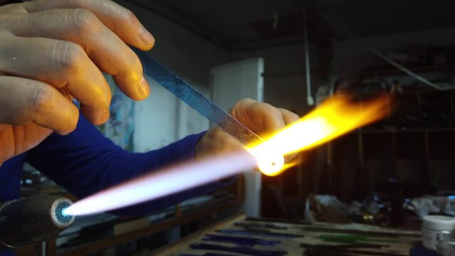  Close up of artist hands creating glass pendant with lampworking technique. Shaping glass with flame making jewelry using gas burner