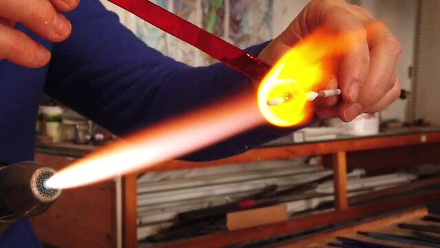 Slow motion view of artist hands creating glass pendant with lampworking technique. Shaping glass with flame making jewelry using gas burner