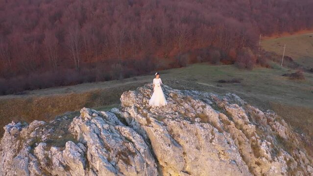  Slow motion aerial view of bride in white wedding dress standing on a cliff