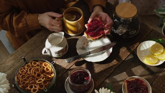 Rustic morning breakfast. Person drinking tea and eating sandwich with berry jam